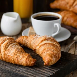 Breakfast with croissants, coffee, orange juice and berries on wooden table. Closeup view, selective focus