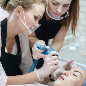 Decorative cosmetology practical training. Female intern using tattoo machine for eyebrow microblading.